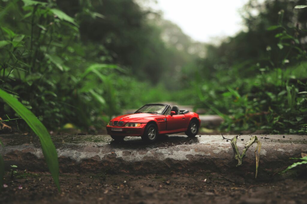 A miniature red convertible toy car placed on a stone surface amidst a lush green forest setting.